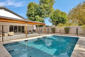 A rectangular swimming pool with a wooden deck and lounge chairs, surrounded by a metal fence and trees. - Casa Biltmore ~ Modern & Luxurious Family Retreat! (Phoenix)