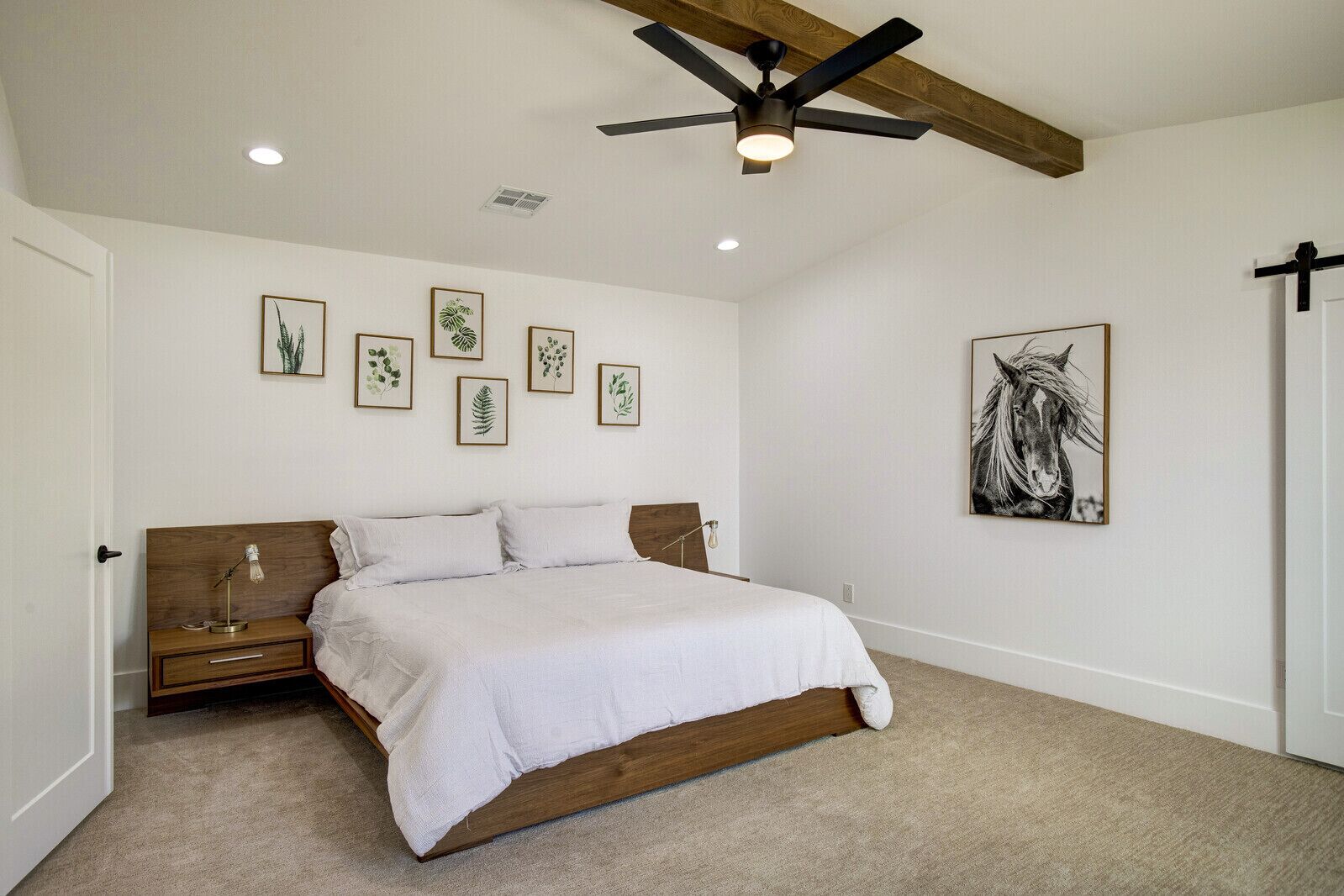 A bedroom with a wooden bed, a ceiling fan, and framed botanical prints on the wall.