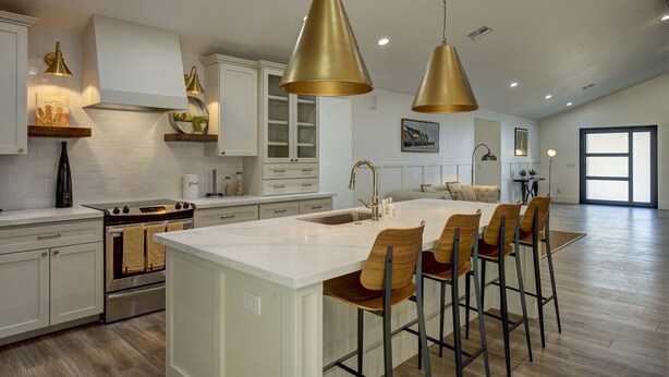 Una cucina moderna con un'isola centrale, sgabelli da bar, illuminazione a sospensione e un'ampia finestra.