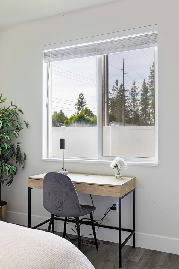 A bedroom with a bed, a desk with a chair, a potted plant, and a window with a view of trees and a fence. - New Modern Townhome- downtown CDA-minutes to waterfront, restaurants, and shops! (Coeur d'Alene)
