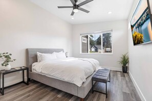 Une chambre moderne avec un lit, un ventilateur de plafond, une fenêtre donnant sur un beau paysage et une petite table agrémentée d’une plante.