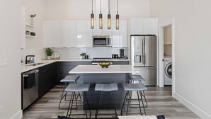 A modern kitchen with white cabinets, a central island with bar stools, a built-in oven, and a stainless steel refrigerator. - New Modern Townhome- downtown CDA-minutes to waterfront, restaurants, and shops! (Coeur d'Alene)