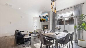 A modern living room with a fireplace, dining area, and a large TV mounted on the wall. - New Modern Townhome- downtown CDA-minutes to waterfront, restaurants, and shops! (Coeur d'Alene)