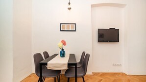 Un coin repas comprenant une table, des chaises, un vase avec des fleurs, un téléviseur fixé au mur et un tableau encadré.