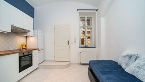 Une cuisine compacte avec des meubles blancs, une cuisinière et un petit plan de travail. On y trouve un lit avec une couverture bleue et un oreiller blanc.