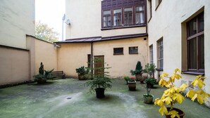 Une cour avec des plantes en pot, un banc et un bâtiment doté d’une fenêtre marron et d’une antenne parabolique.
