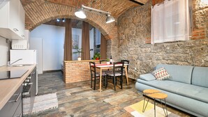 A cozy kitchen with a dining area, stone walls, and a modern sofa.