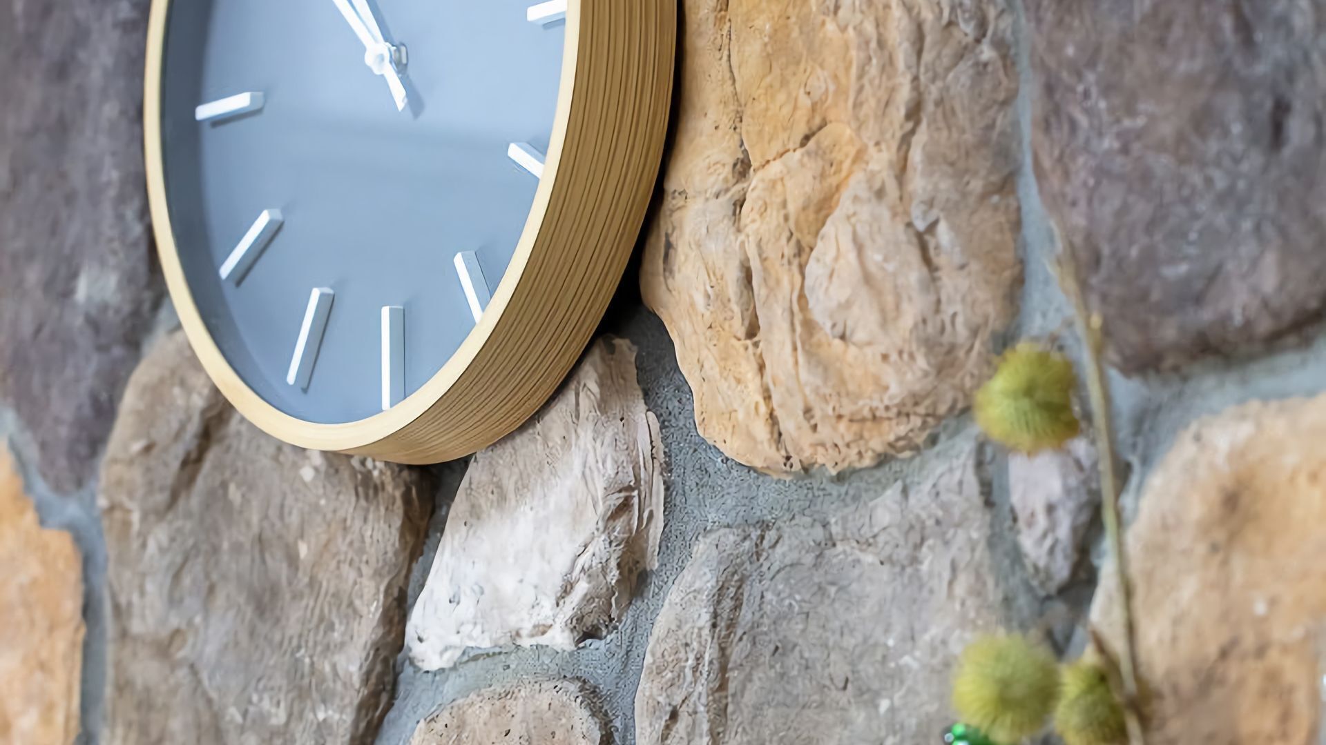 A clock with a wooden frame mounted on a stone wall.