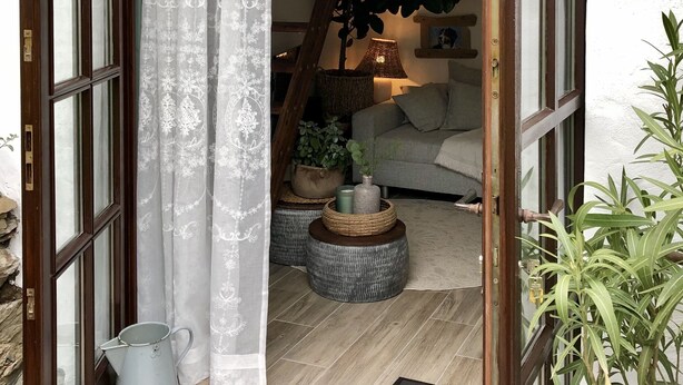 En indgang med en trædør, et hvidt gardin, en trappe, en sofa og en plante.