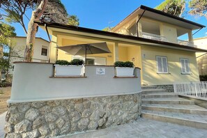 Un bâtiment à deux étages, avec une base en pierre, un balcon et un escalier menant à l’entrée.
