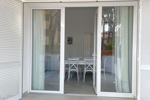 Une porte-fenêtre coulissante donnant sur un balcon agrémenté de chaises blanches et d’une petite table.