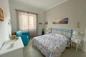 Une chambre à coucher avec un lit, une chaise bleue, une petite table et une fenêtre avec des rideaux.