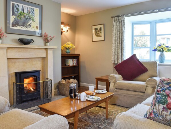 A cozy living room with a fireplace, a bookshelf, a coffee table with breakfast items, and a window with curtains.