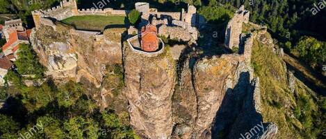 Une vue aérienne d’un château historique perché au sommet d’une falaise, entouré d’une forêt dense.