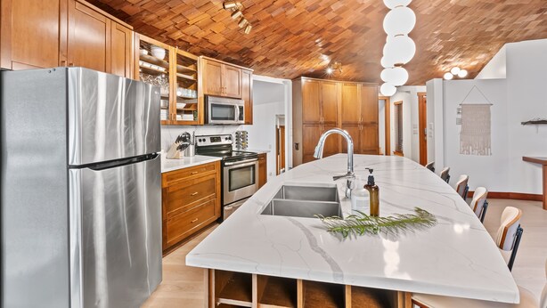 Cocina moderna con techo de madera, electrodomésticos de acero inoxidable y una isla grande con fregadero.