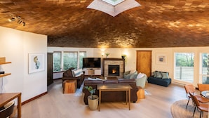 Un amplio salón con techo abovedado, chimenea y un ventanal con vistas a zonas verdes.