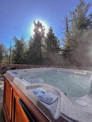 A hot tub with a wooden exterior, surrounded by trees and a clear sky.