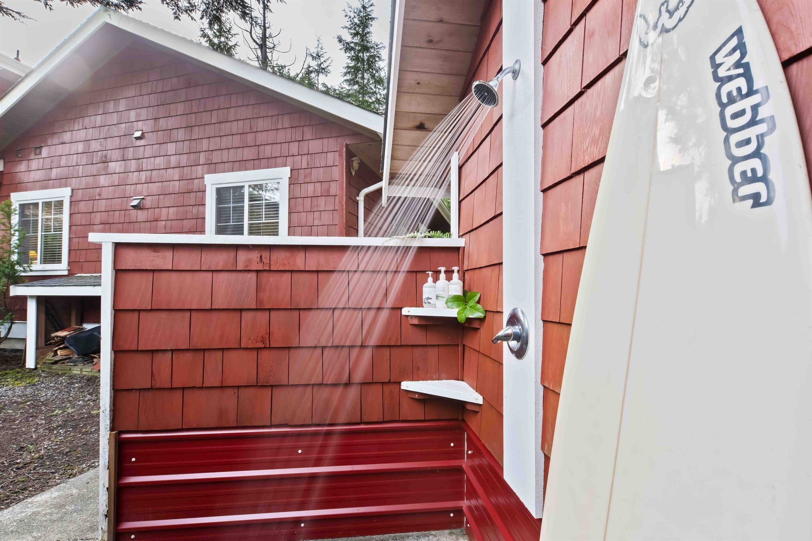 Una casa de madera roja con una puerta blanca, una escalera roja y una tabla de surf blanca con la palabra 'Webber'.