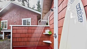 A red wooden house with a white door, a red staircase, and a white surfboard with the word "Webber" on it. - Coastal Haven-N Chesterman Beach, Hot Tub, Surf! (Tofino)