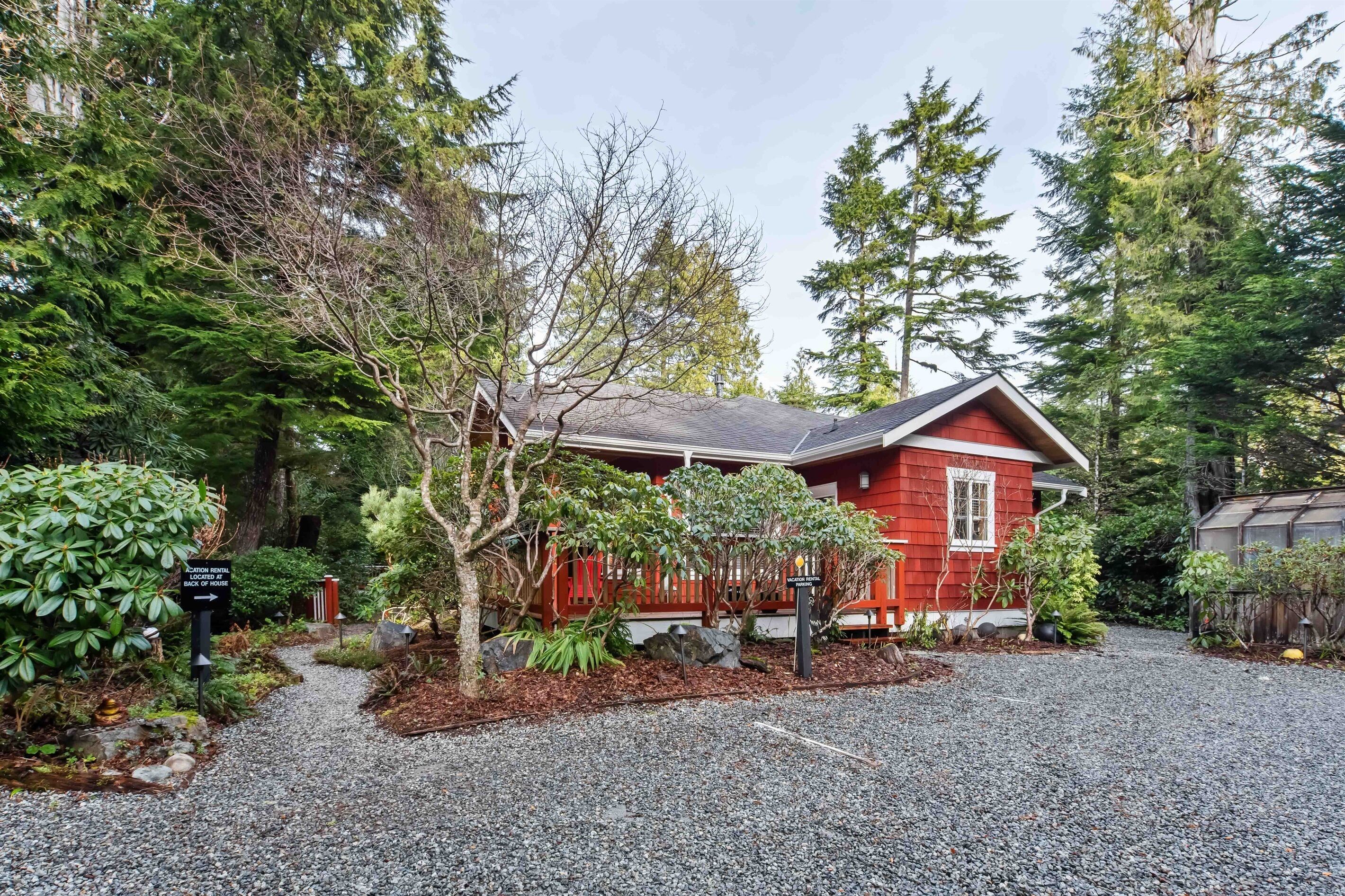 A red cabin with a gravel driveway, surrounded by dense forest and a sign indicating a reservation booking area.