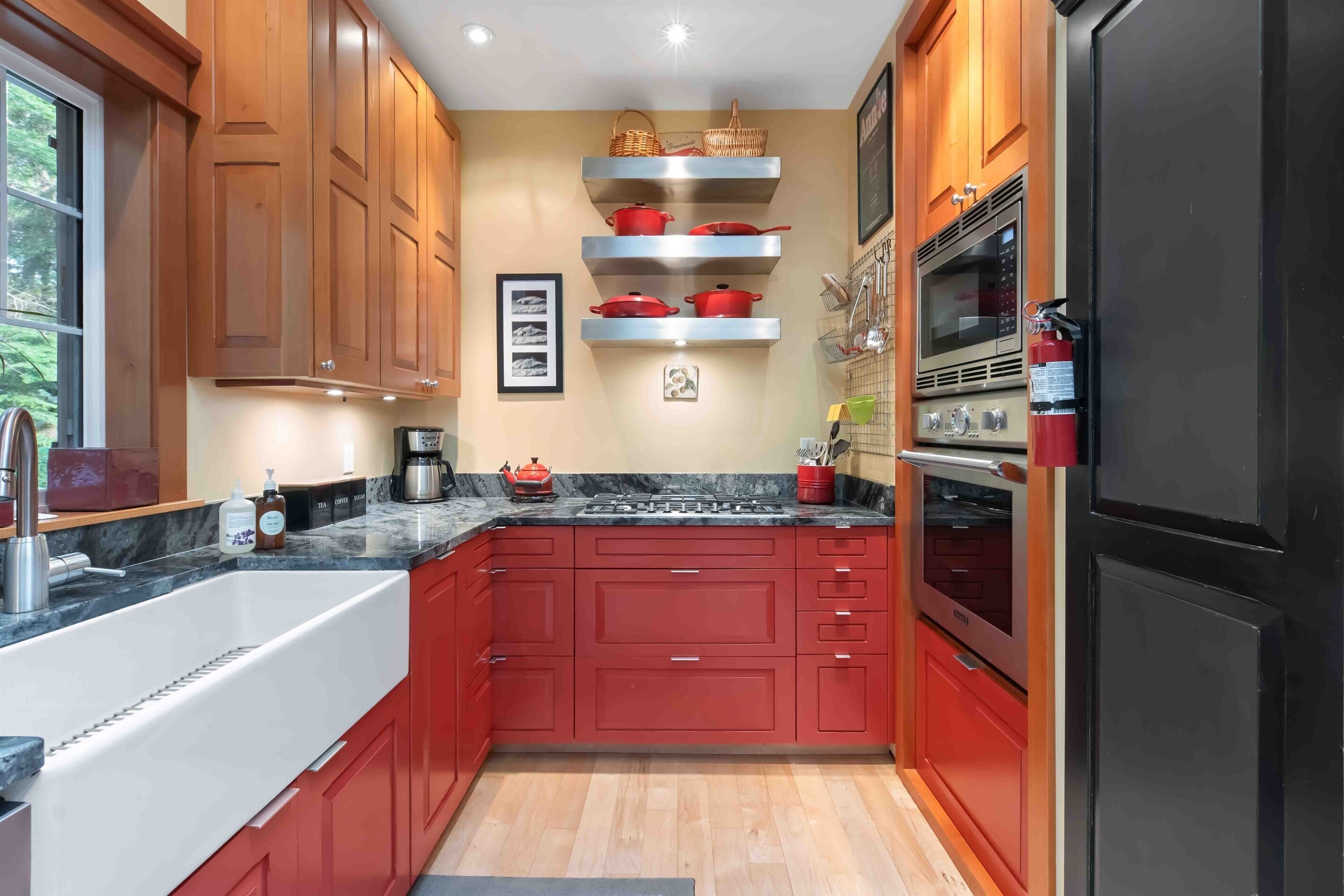 Una cocina moderna con armarios rojos, un lavamanos de acero inoxidable y un horno empotrado.
