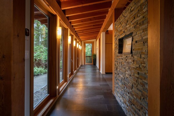 A corridor with wooden beams, large windows, and a stone wall. - Coastal View-Rated top place to stay on the inlet! (Tofino)