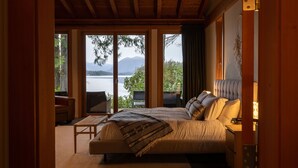 A bedroom with a large bed, a small table, and a view of a lake and mountains. - Coastal View-Rated top place to stay on the inlet! (Tofino)