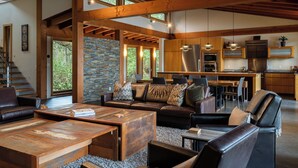 A spacious living area with a fireplace, wooden beams, and a kitchen in the background. - Coastal View-Rated top place to stay on the inlet! (Tofino)
