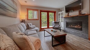 A modern living room with a sofa, a fireplace, a television, and a large window.