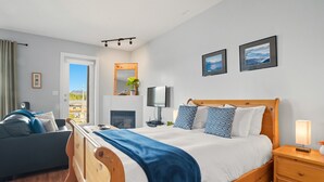 A bedroom with a wooden bed, a TV, a bedside table with a lamp, a sofa, a fireplace, and a view of the outdoors. - Fred Tibbs #10-Ocean View, D.T, Fireplace, Pets (Tofino)