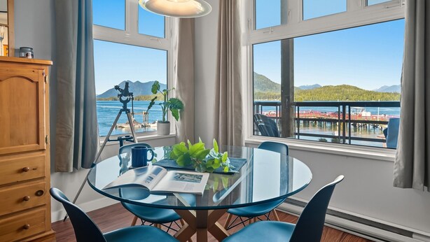 A room with a glass table, blue chairs, a wooden cabinet, a tripod, and a potted plant. - Fred Tibbs #10-Ocean View, D.T, Fireplace, Pets (Tofino)