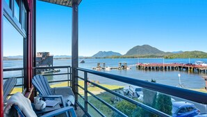 A balcony with seating, a view of a docked boat, and a mountain in the distance. - Fred Tibbs #10-Ocean View, D.T, Fireplace, Pets (Tofino)