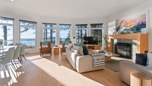A spacious living room with a large TV, a fireplace, and a dining area with a view of the ocean.