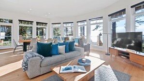 A modern living room with a grey sofa, blue cushions, a wooden coffee table, and a large TV.