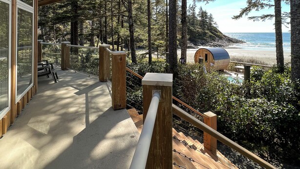 A wooden deck with a glass wall overlooking a forest and a beach.