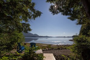 A lakeside view with a wooden deck, two blue chairs, and a rocky shoreline. - Orca View House-Inlet, Mackenzie Beach, Downtown (Tofino)