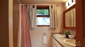 Une salle de bain avec un rideau de douche, une fenêtre, un lavabo, un miroir et un porte-serviettes.