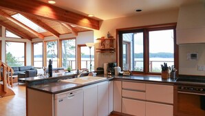 Une cuisine moderne dotée d’un îlot central, de grandes fenêtres et offrant une vue sur un lac.