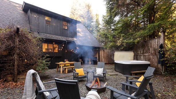 Un patio trasero con terraza de madera, mobiliario exterior, un pozo de fuego y un jacuzzi.