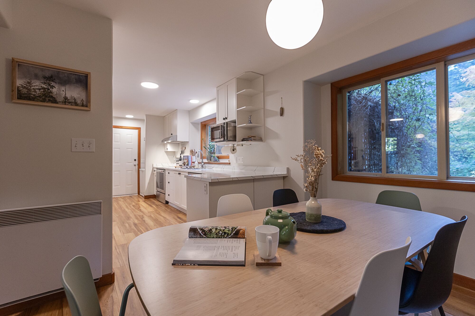 A modern kitchen with white cabinets, a central island, and a dining area with a round table and chairs.