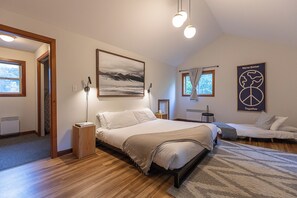 Ein Schlafzimmer mit einem großen Bett, einem Einzelbett, einem Schreibtisch und einem Stuhl. Es gibt ein Fenster mit Vorhängen, ein Wandbild und einen Poster an der Wand.