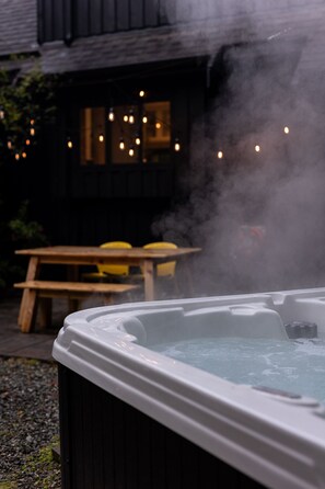 Ein Whirlpool mit aufsteigendem Dampf, ein Holztisch und Stühle im Hintergrund.