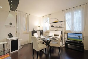 A dining area with a round table, four chairs, a TV, and a small kitchen area with a refrigerator and a shelf. - Downtown Apartment (Salò)