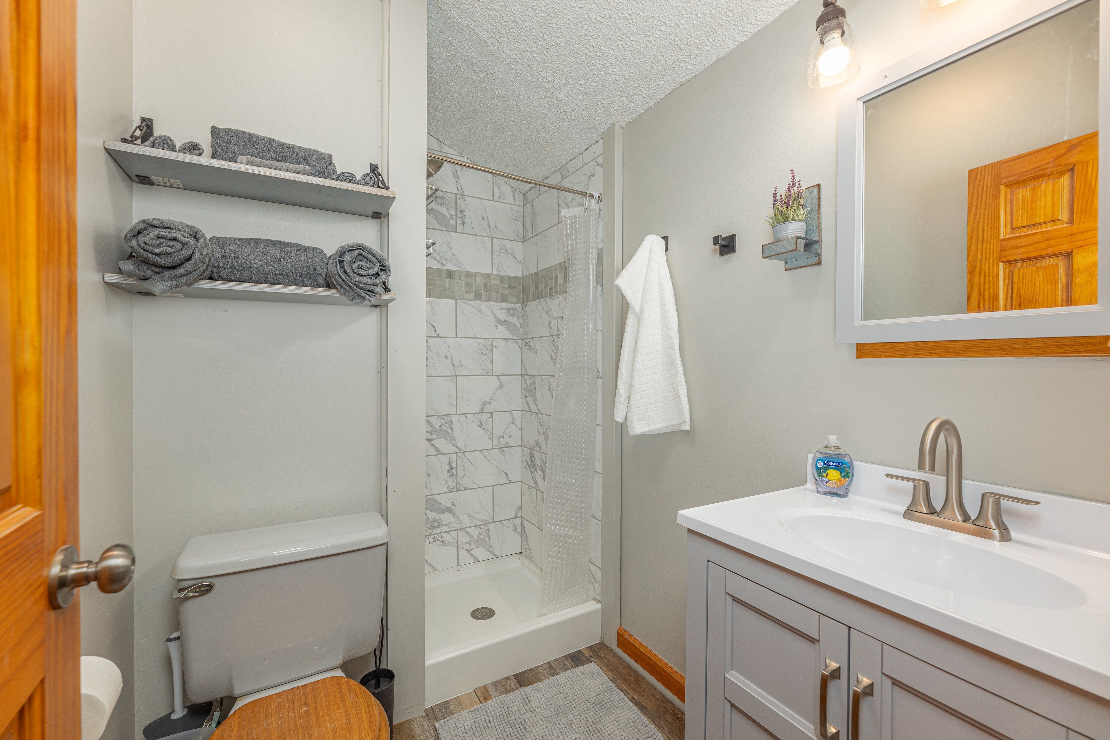 A bathroom with a toilet, shower, and sink. There are shelves with towels and a mirror above the sink.