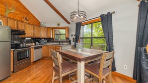 A kitchen with wooden cabinets, a stainless steel refrigerator, a wooden dining table with chairs, and a hanging light fixture. - Spectacular Smoky Mtn. Views from Oversized Hot Tub Close to Downtown Gatlinburg (Gatlinburg)