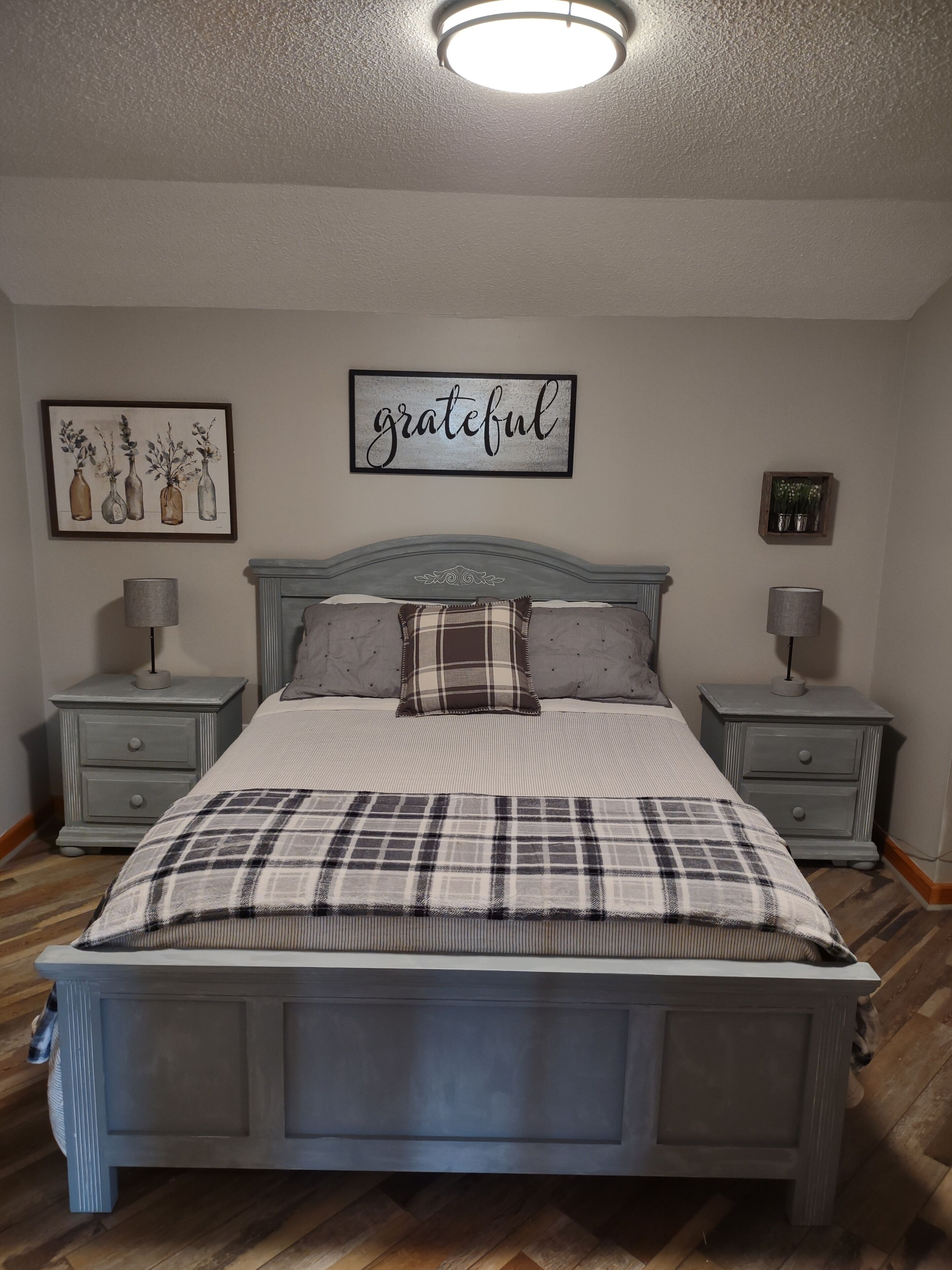 Ein Schlafzimmer mit einem Bett, zwei Nachttischen, einer Wandleuchte, einem gerahmten Kunstwerk und einer Deckenlampe.