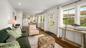 A spacious living room with a green sofa, a wooden coffee table, and a dining area with a kitchen in the background. - *NEW Poipu 2BR Retreat|Pool|AC & Athletic Club (Koloa)