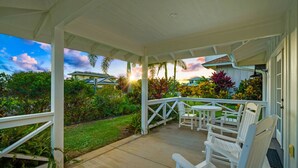 A covered outdoor area with white chairs and a table, surrounded by lush greenery and a view of a building with a blue roof. - *NEW Poipu 2BR Retreat|Pool|AC & Athletic Club (Koloa)