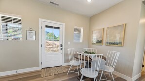 A dining area with a white table and chairs, a door with a view, and two framed pictures on the wall. - BLACK SHEEP INN Newly Constructed Suffolk #2 of 4 Units  (Cedar City)