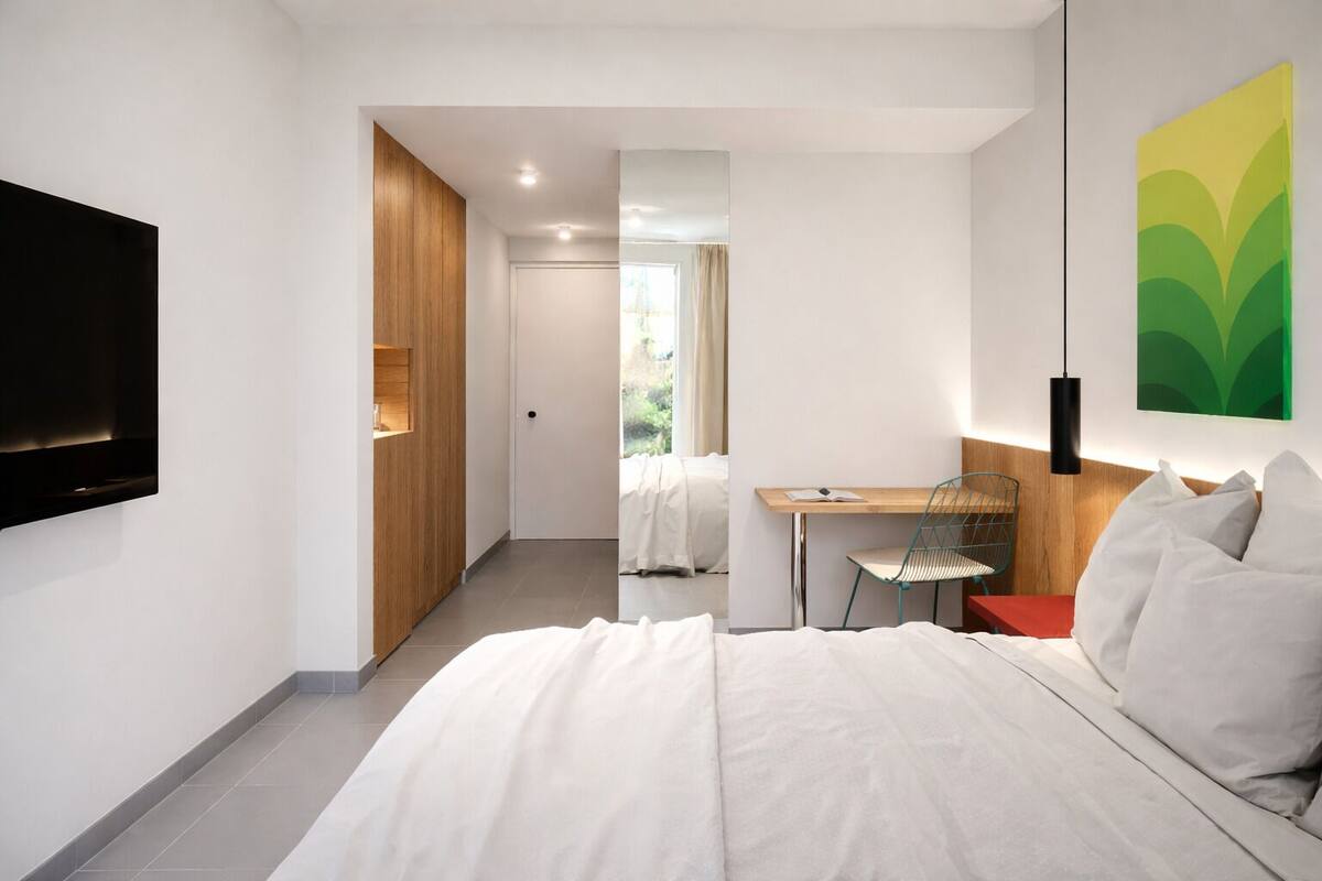 Una habitación de hotel moderna con una cama grande, un escritorio, una silla y un televisor fijado a la pared.